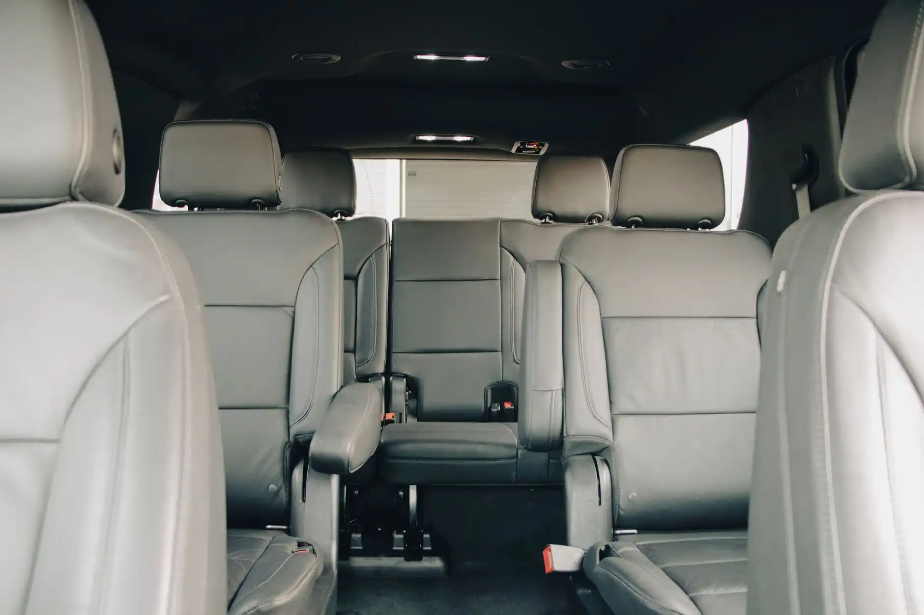 Detailed interior of a clean Cadillac Escalade with black leather captain’s chairs, bottled water, luggage area, and Seattle airport signage visible outside